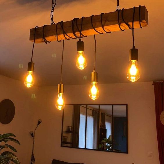 Vintage-style hanging light fixture with five glowing Edison bulbs in a cozy living room setting with warm decor.