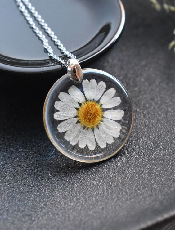 Silver necklace with a daisy pendant in a glass dome, delicately placed on a black ceramic dish.