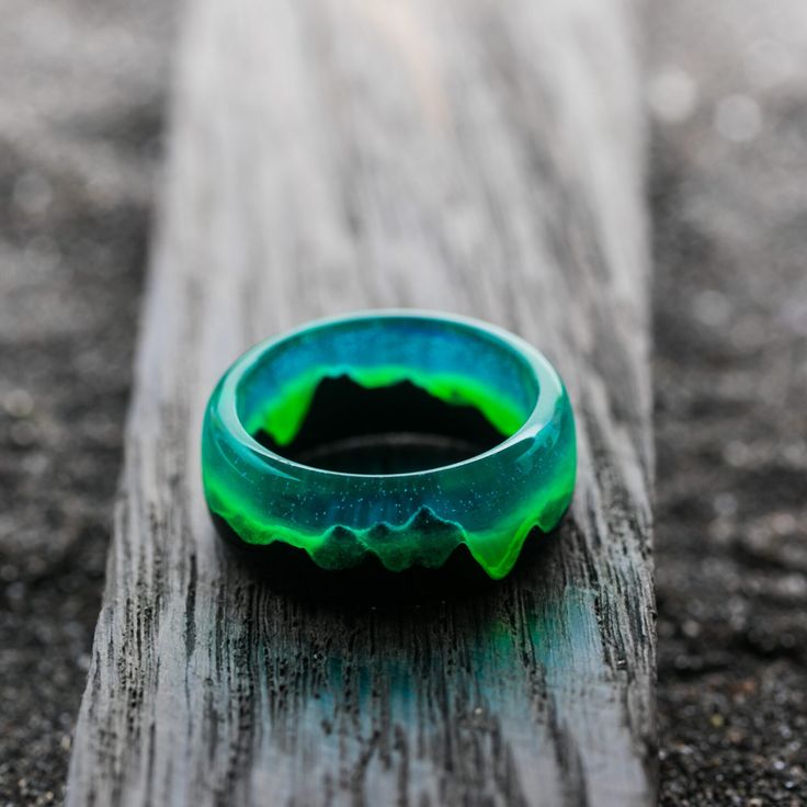 Close-up of a luminous green resin ring with mountain design placed on a wooden surface. Unique, handmade jewelry.