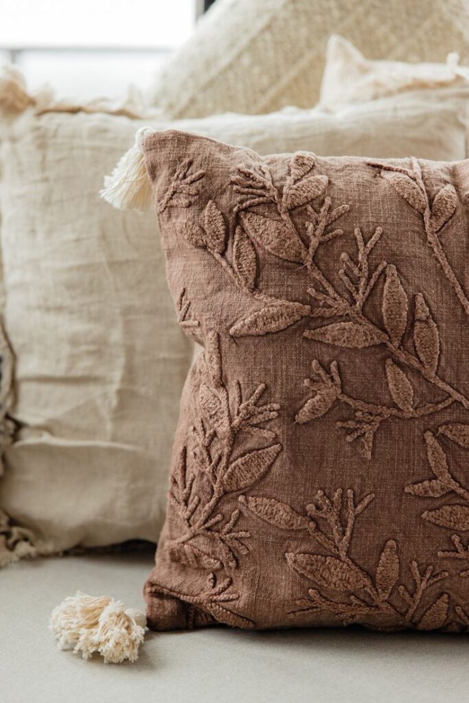 Close-up of a brown decorative throw pillow with embroidered leaf pattern, accented by beige pillows in the background.