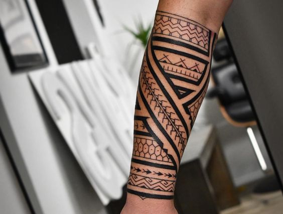 Forearm with an intricate tribal tattoo design featuring bold black lines and geometric patterns in a modern tattoo studio.