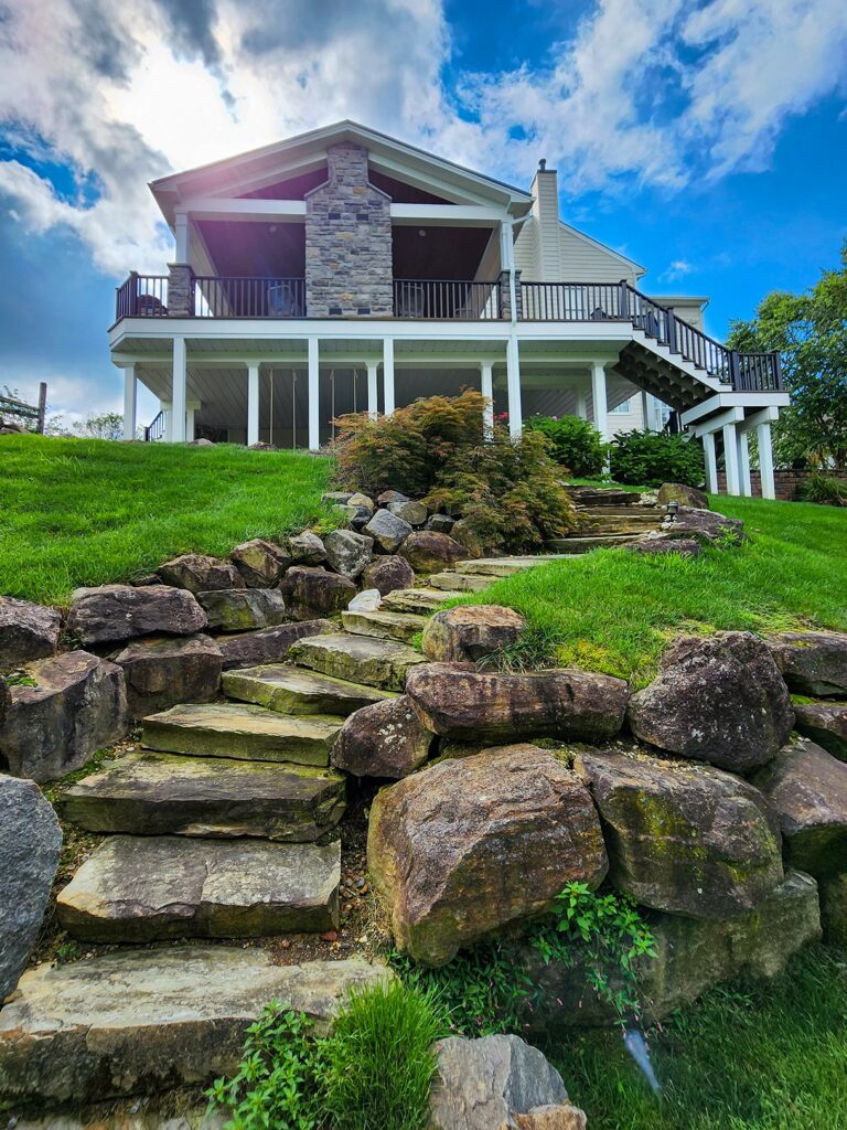 Modern home with stone pathway, lush green lawn, and vibrant blue sky. Exterior view highlighting natural landscaping.