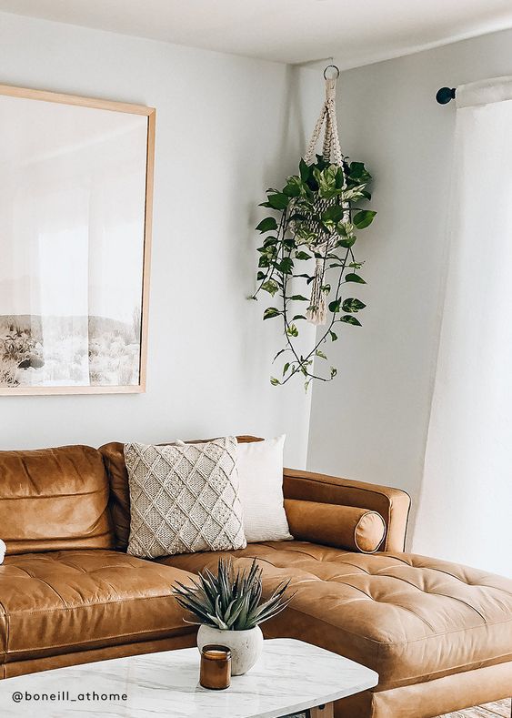 Modern living room with a brown leather sofa, indoor plants, and a white marble coffee table with decor accessories.