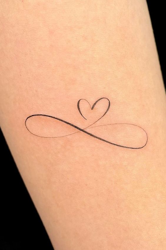 Minimalist infinity symbol tattoo with a heart on skin, representing eternal love and connection.