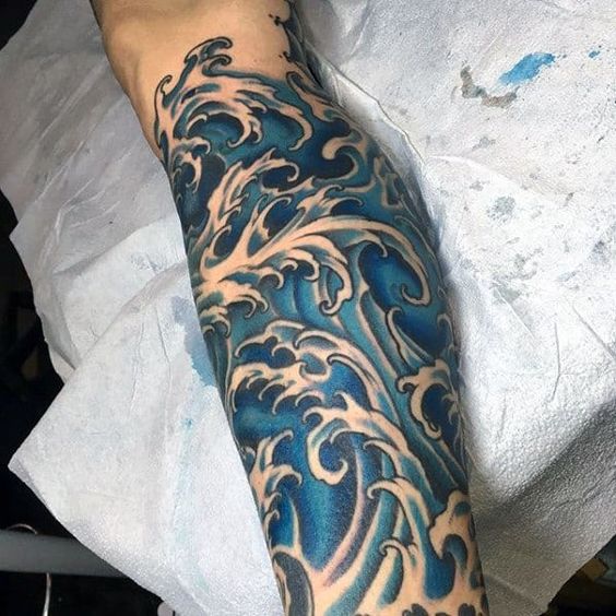 Close-up of a vibrant blue wave tattoo sleeve on an arm, featuring intricate ocean wave designs with a realistic aesthetic.