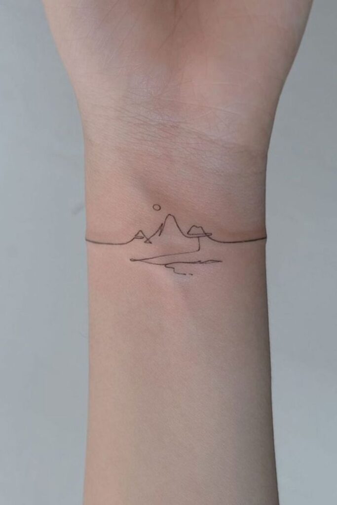 Minimalistic wrist tattoo featuring a fine line mountain range with a sun and a wave, representing nature and adventure.