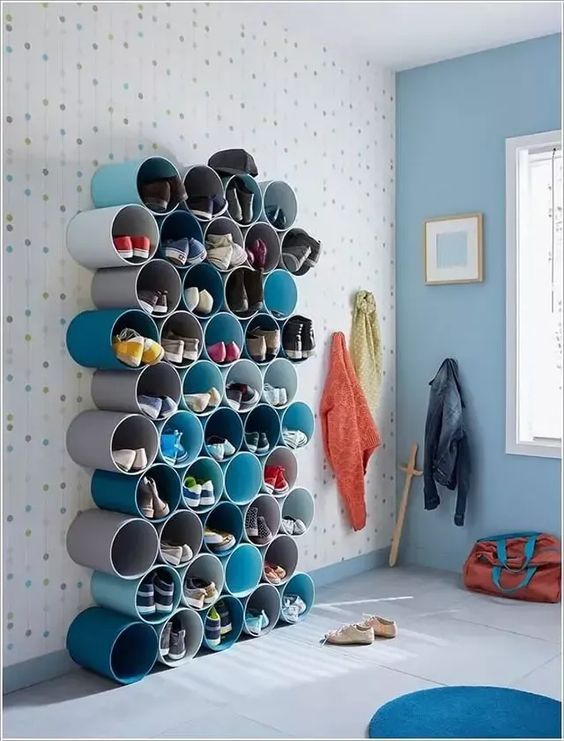 Creative shoe storage solution using cylindrical shelves in a modern and colorful room with coats and bags hanging nearby.