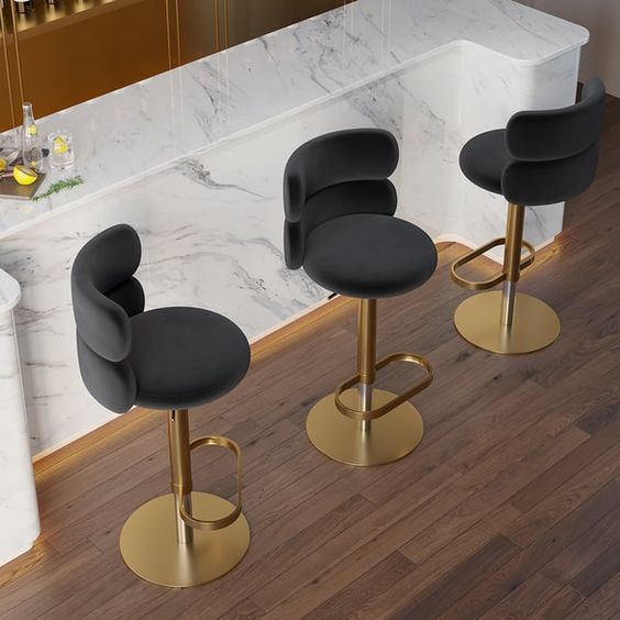 Modern bar stools with gold bases and black seats in front of a marble countertop in a stylish bar setting.