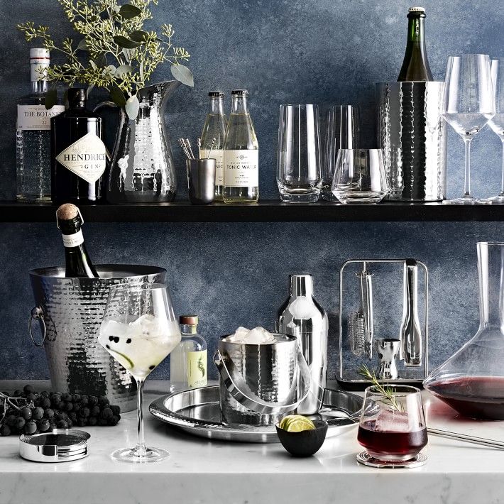 Sophisticated home bar setup with gin, tonic, wine glasses, shaker, ice bucket, decanter, and garnished cocktails on marble counter.