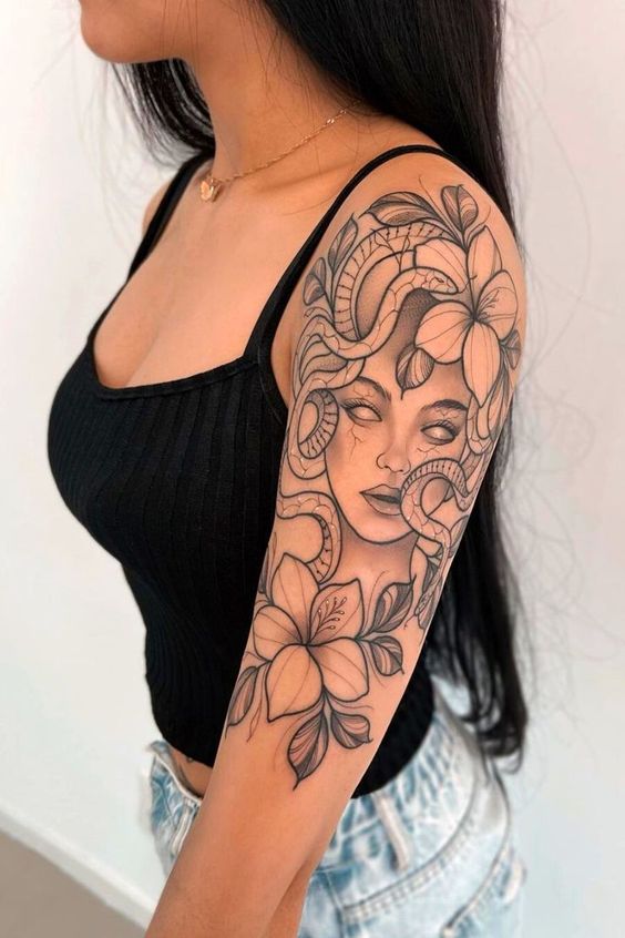 Woman with detailed Medusa-themed tattoo featuring snakes and flowers on her upper arm, wearing a black tank top.