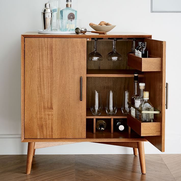 Mid-century modern wooden bar cabinet with glassware, liquor bottles, and barware accessories on top.