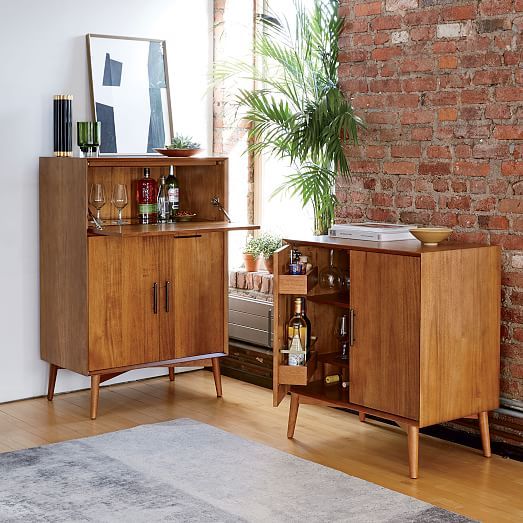 Mid-century modern wooden bar cabinets with liquor bottles and plants against an exposed brick wall background in a stylish home.