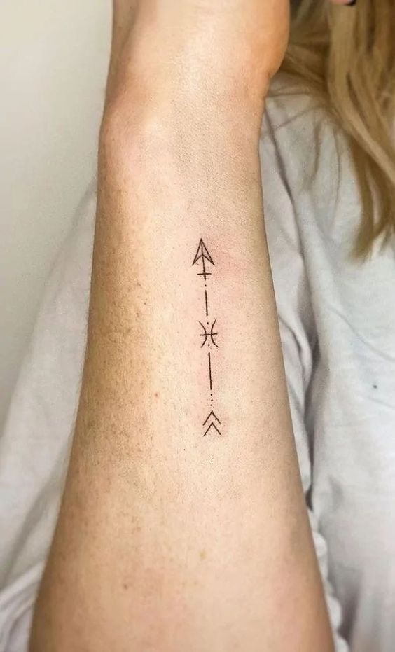 Minimalist arrow tattoo with geometric lines on an inner forearm, featuring delicate dots and abstract designs.