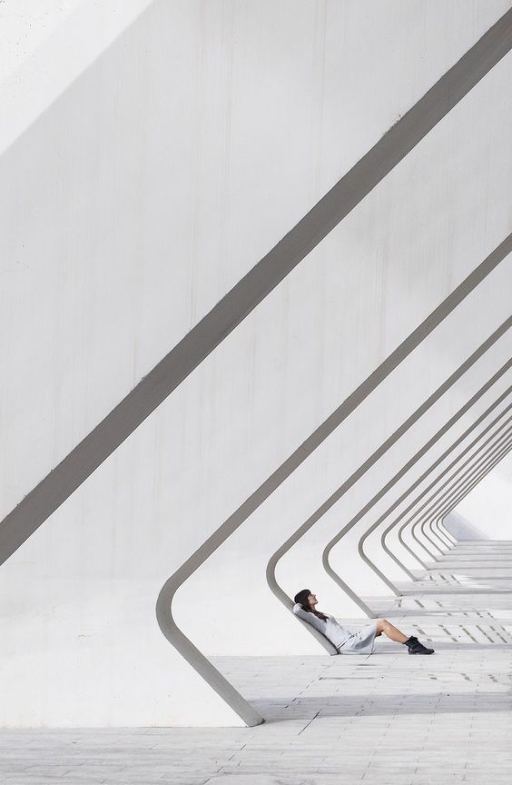 Person relaxing on a futuristic white architectural structure with repeating geometric patterns and shadows.