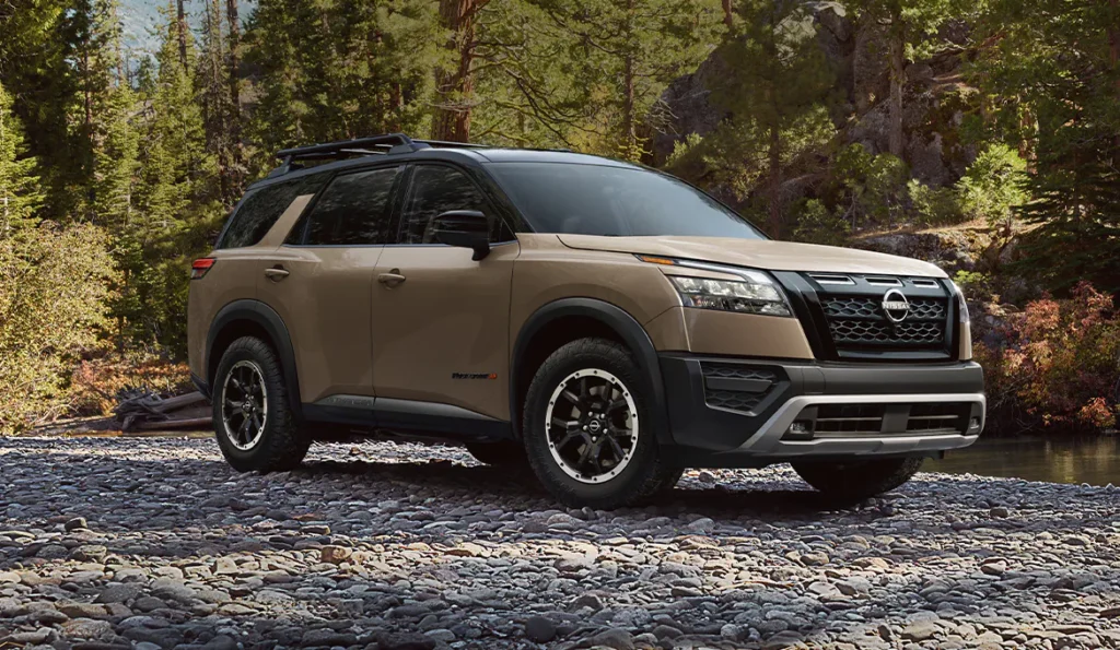 Nissan Pathfinder SUV parked on rocky terrain in a forest, showcasing its rugged design and off-road capability.