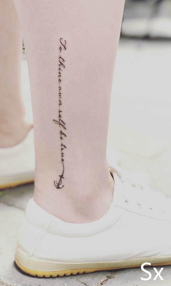 Elegant ankle tattoo with the script To thine own self be true and an anchor design, displayed on pale skin in white shoes.