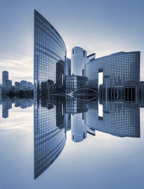 Modern skyscrapers reflecting on water at sunrise, displaying sleek architectural design and urban cityscape.