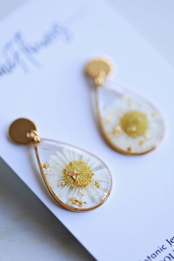 Gold floral resin earrings with white daisies and gold flakes, teardrop shape and circular posts, delicate botanical jewelry.