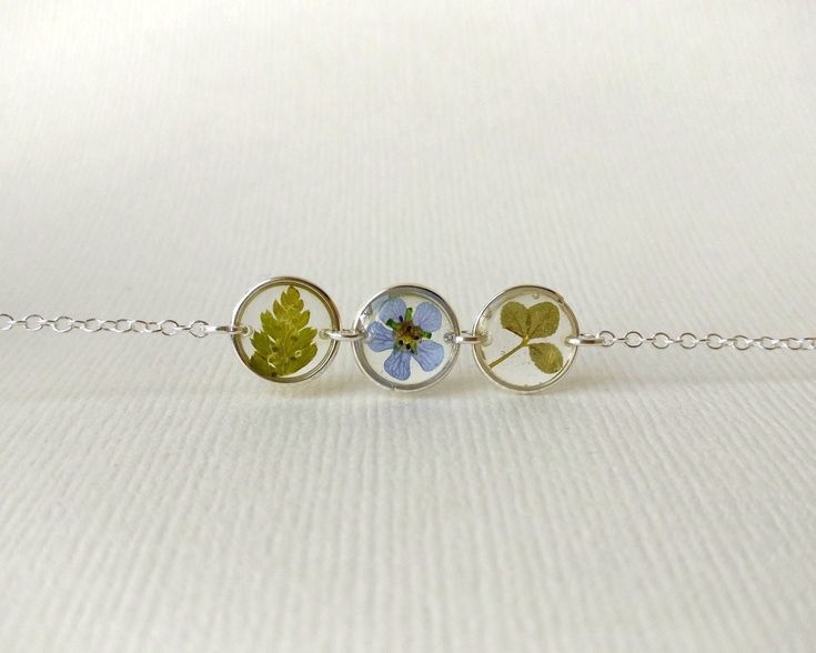 Silver bracelet with three circular charms, featuring pressed fern, blue flower, and clover leaf on a light background.