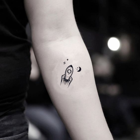 Minimalistic rocket ship tattoo on inner arm with stars and a crescent moon, symbolizing space exploration and adventure.