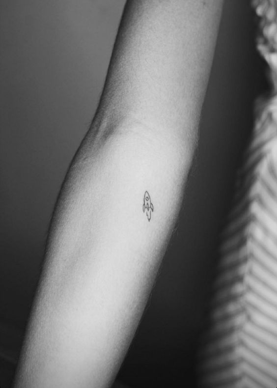 Minimalist rocket ship tattoo on inner forearm, black ink, small design, symbolic of exploration and adventure.