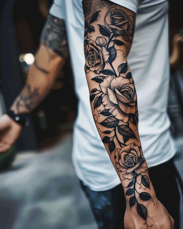 Detailed black and grey rose sleeve tattoo on person's arm wearing a white t-shirt.