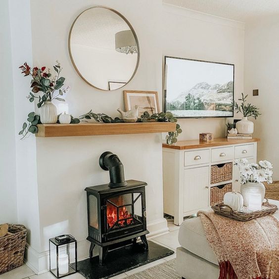 Cozy living room with a modern electric fireplace, round mirror, and farmhouse decor, featuring a mountain landscape painting.