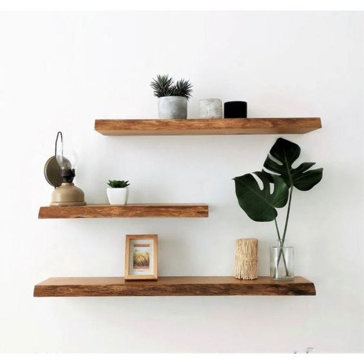 Wooden floating shelves with potted plants, decorative items, and a framed picture on a white wall. Minimalist home decor.