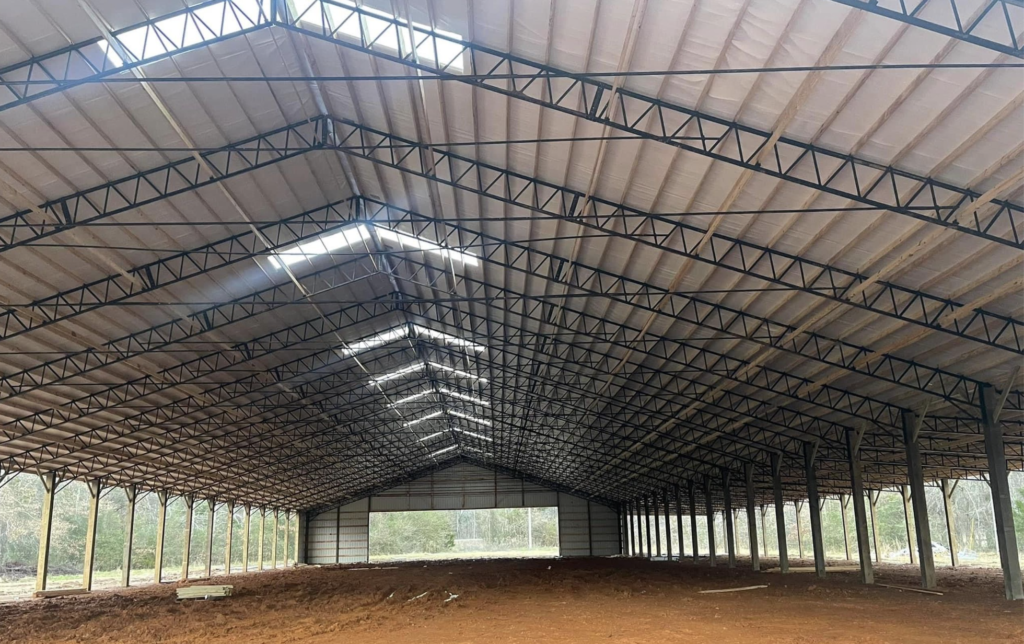 Interior view of a large industrial warehouse with steel roofing structure and open roll-up doors.