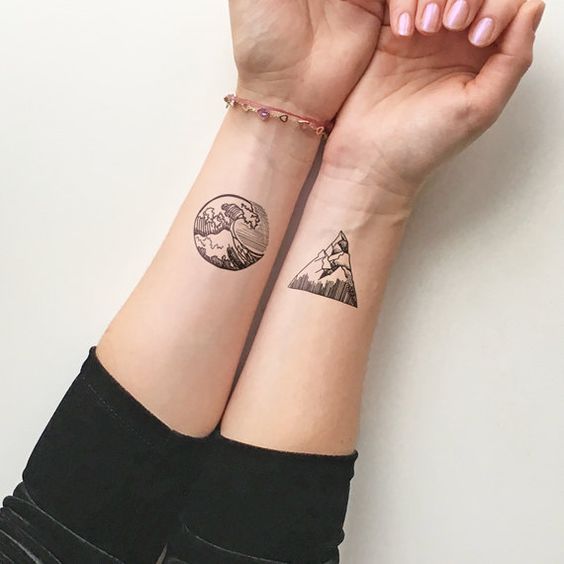 Two forearm tattoos: one circular with a wave design, and one triangular with a mountain design, displayed on wrists.