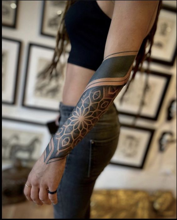 Woman showcasing intricate floral forearm tattoo in a studio setting, featuring geometric and blackwork designs.