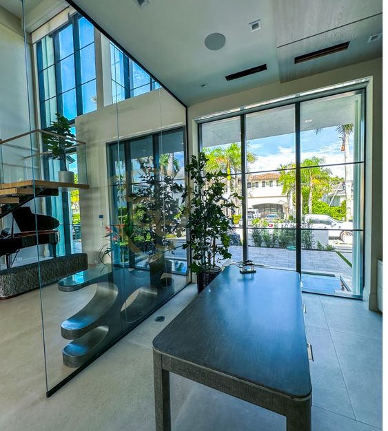 Modern office space with glass walls, large windows, natural light, indoor plants, and a sleek desk.