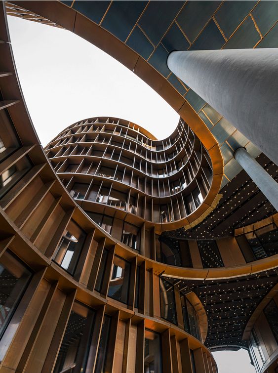 Modern architecture: looking up at a wavy, cylindrical building with striking curves and metal accents.