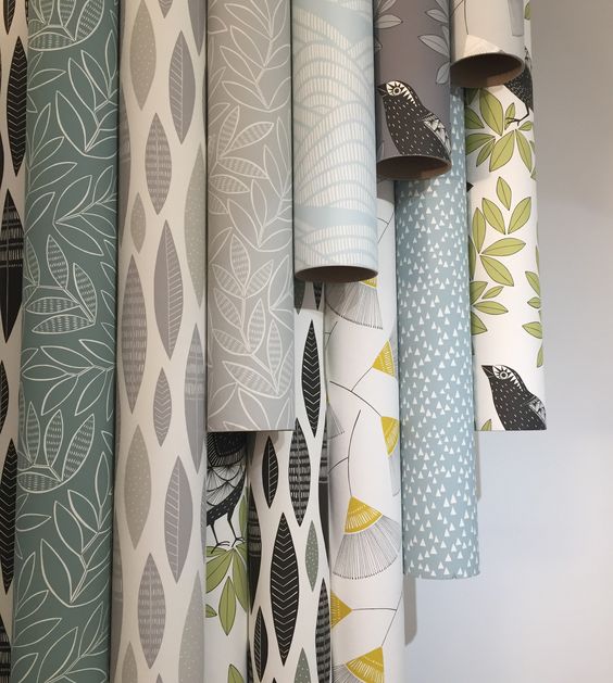 Assorted colorful, patterned wallpaper rolls with botanical and geometric designs hanging on display in a home decor store.