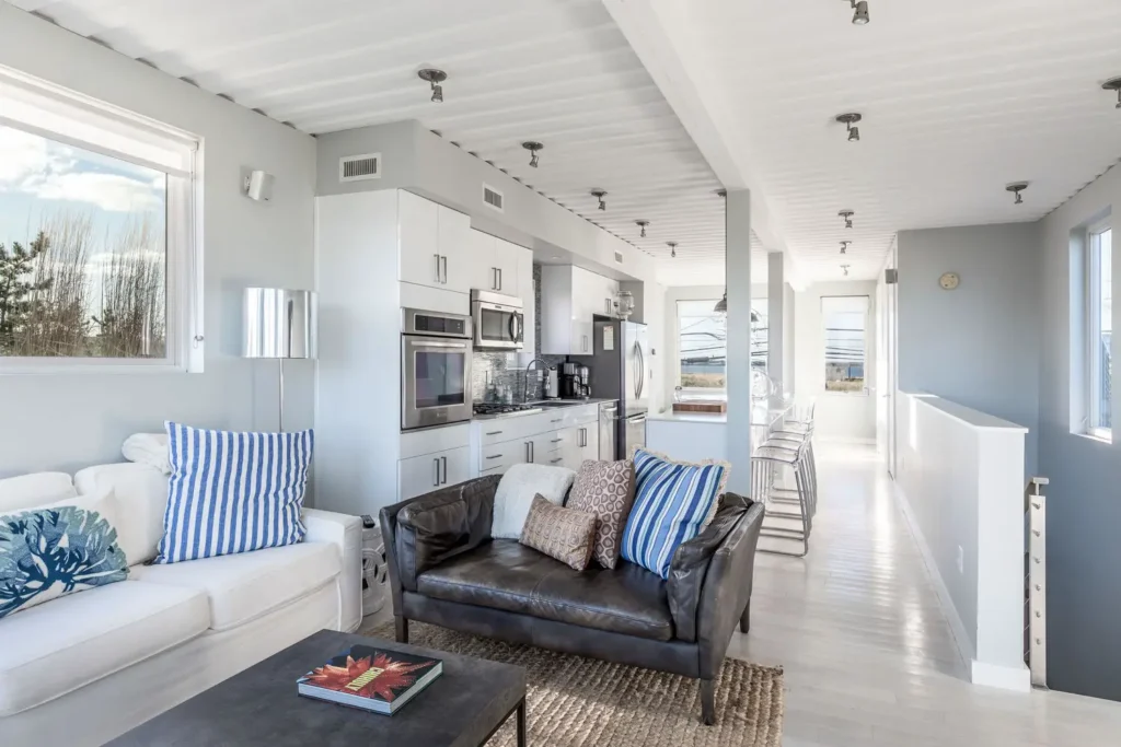 Modern open-plan living room and kitchen with sleek decor, white cabinetry, stainless steel appliances, and comfortable seating.