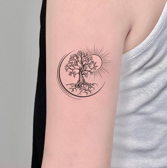 Minimalist tree of life tattoo on upper arm with sun and crescent moon elements, symbolizing nature and balance.