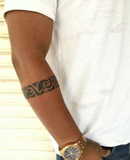 Close-up of a forearm tattoo featuring intricate tribal design with man wearing a white shirt and gold watch.