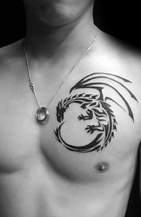 Man with a tribal dragon tattoo on his chest wearing a necklace in black and white image.