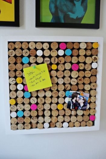 Decorative cork board with colorful pins displaying a sticky note and photo, wall art in the background.