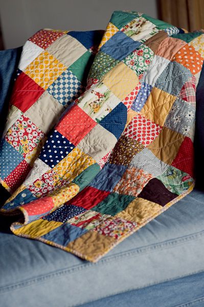 A colorful patchwork quilt with various patterns and fabrics draped over a blue couch for a cozy, homey atmosphere.