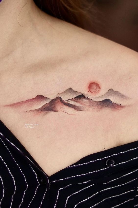 Minimalist mountain and sun tattoo located on the upper chest, showcasing a serene landscape with soft shading.