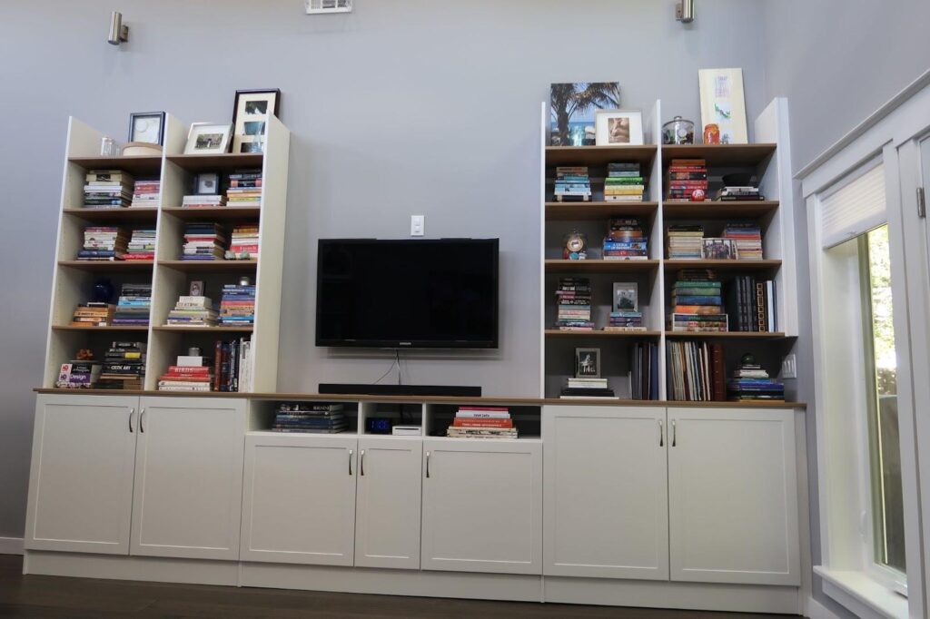 Built-in white bookshelves with a wall-mounted TV in the center, filled with books, decor, and framed pictures.