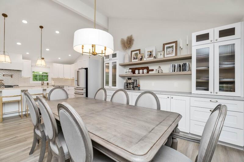 Bright, modern kitchen with a large dining table, sleek white cabinets, and contemporary lighting fixtures.