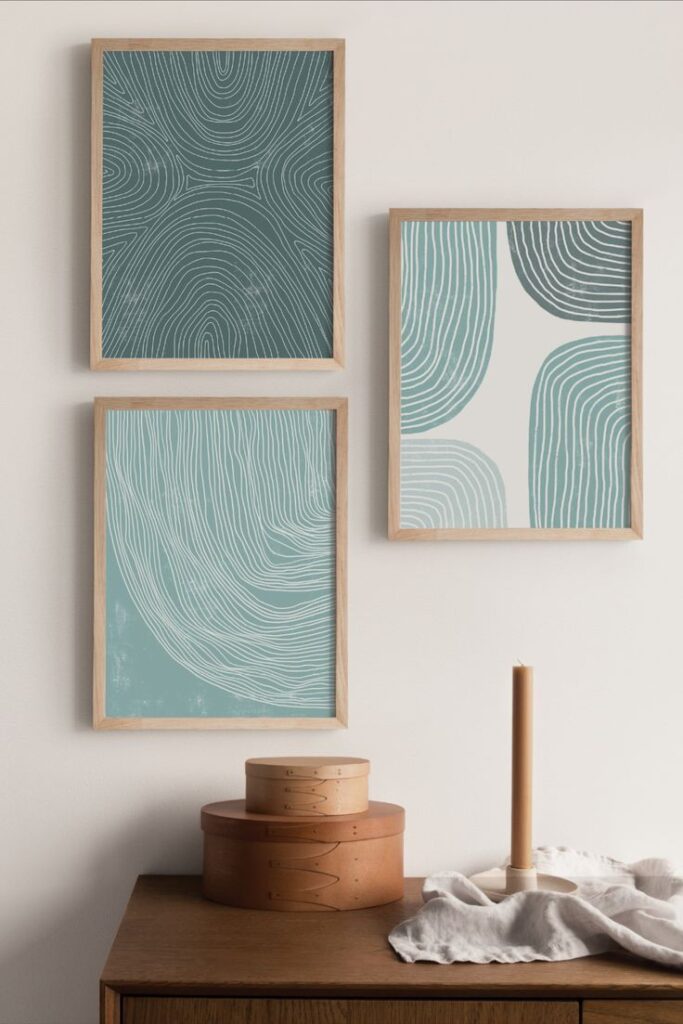 Three framed abstract wall arts with wavy line patterns above a wooden dresser, decorated with boxes and a candle.