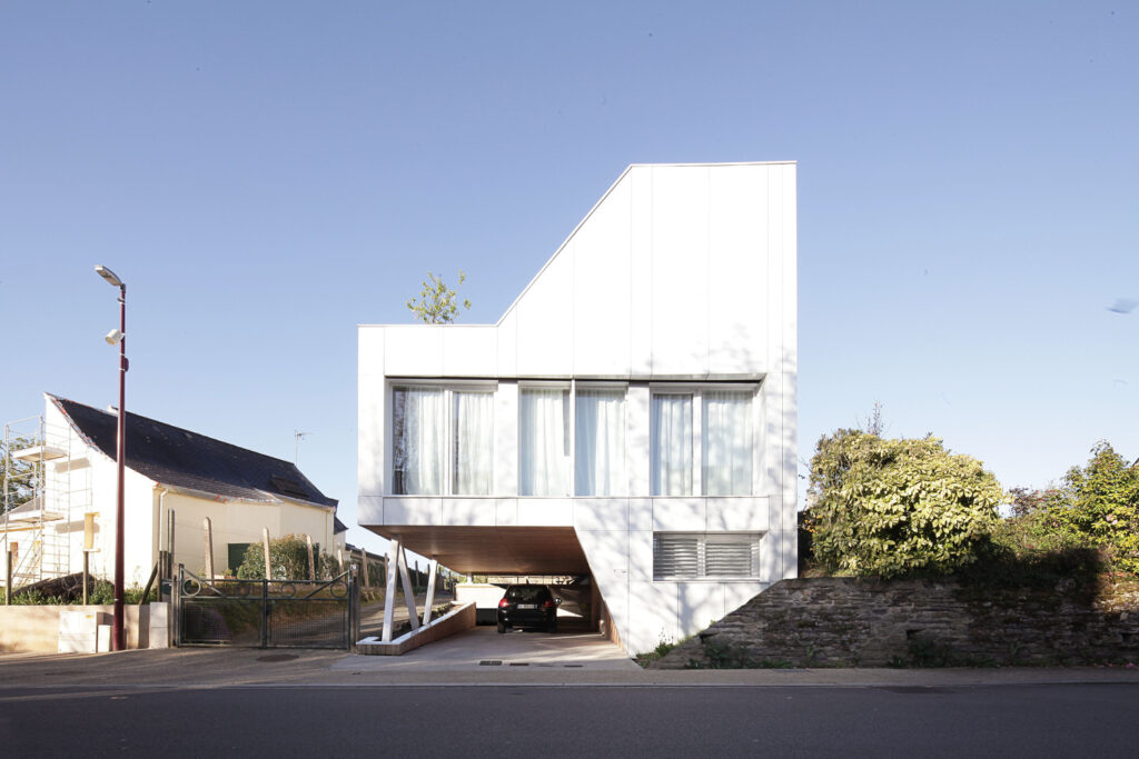 Modern, minimalist, white house with elevated design, carport underneath, large windows, and clear blue sky.