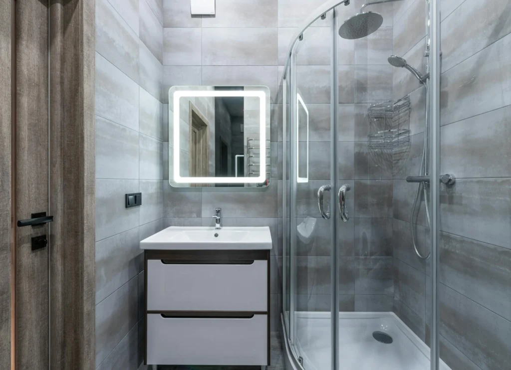 Modern bathroom with glass shower, illuminated mirror, and sleek vanity sink in neutral tones.