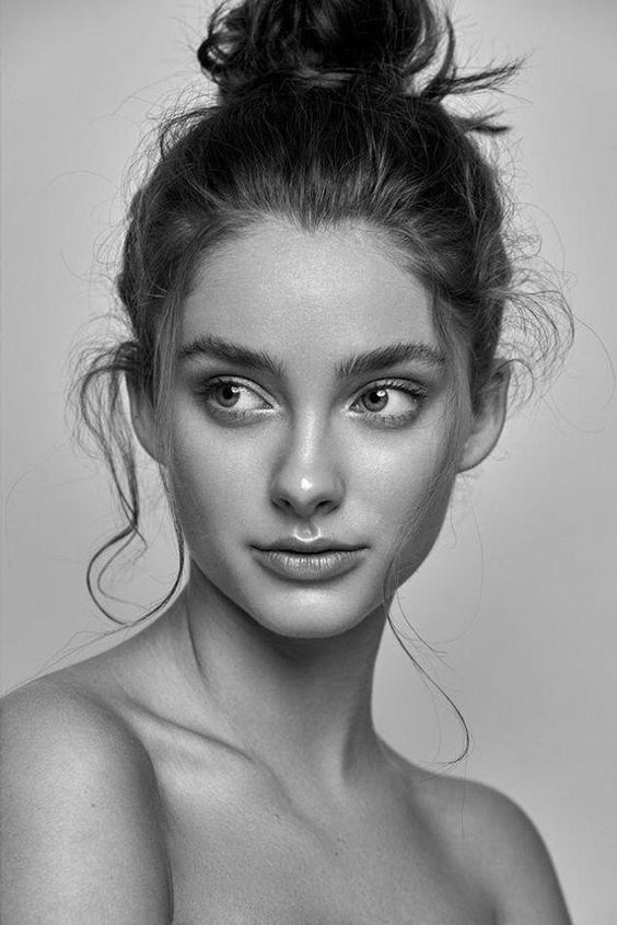 Black and white portrait of a young woman with tousled hair in a bun, looking sideways with a serene expression.