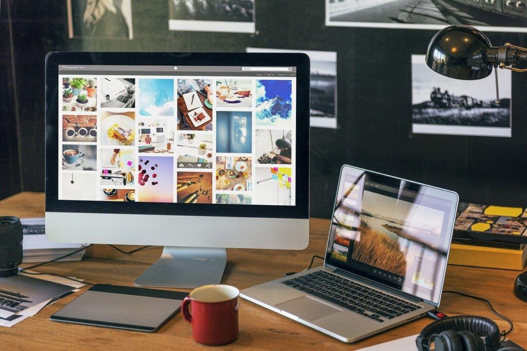 Dual monitors on a stylish workspace desk with a red coffee mug, displaying various colorful images for creative inspiration.