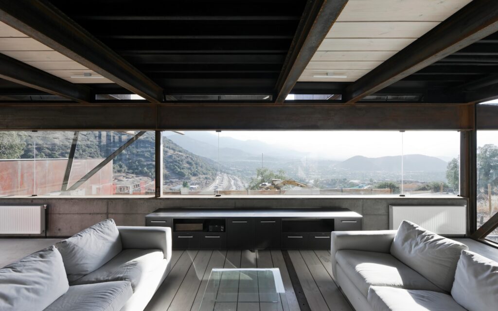 Modern living room with large windows offering a stunning mountain view, wooden floors, neutral sofas, and sleek furniture.