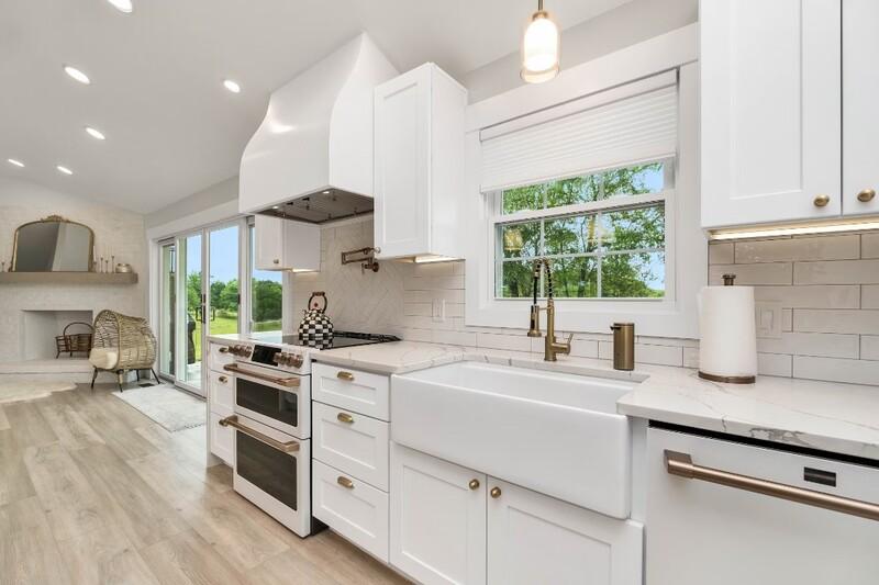 Modern white kitchen with farmhouse sink, stainless steel appliances, and large window offering a view of the outdoors.